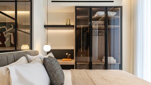 A modern hotel room with a large bed, a bedside table with a lamp, a wardrobe, and a mirror.