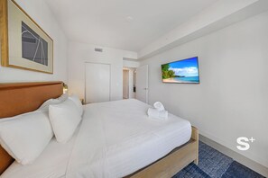 Une chambre d’hôtel avec un grand lit, un téléviseur fixé au mur et un tableau encadré au-dessus du lit.