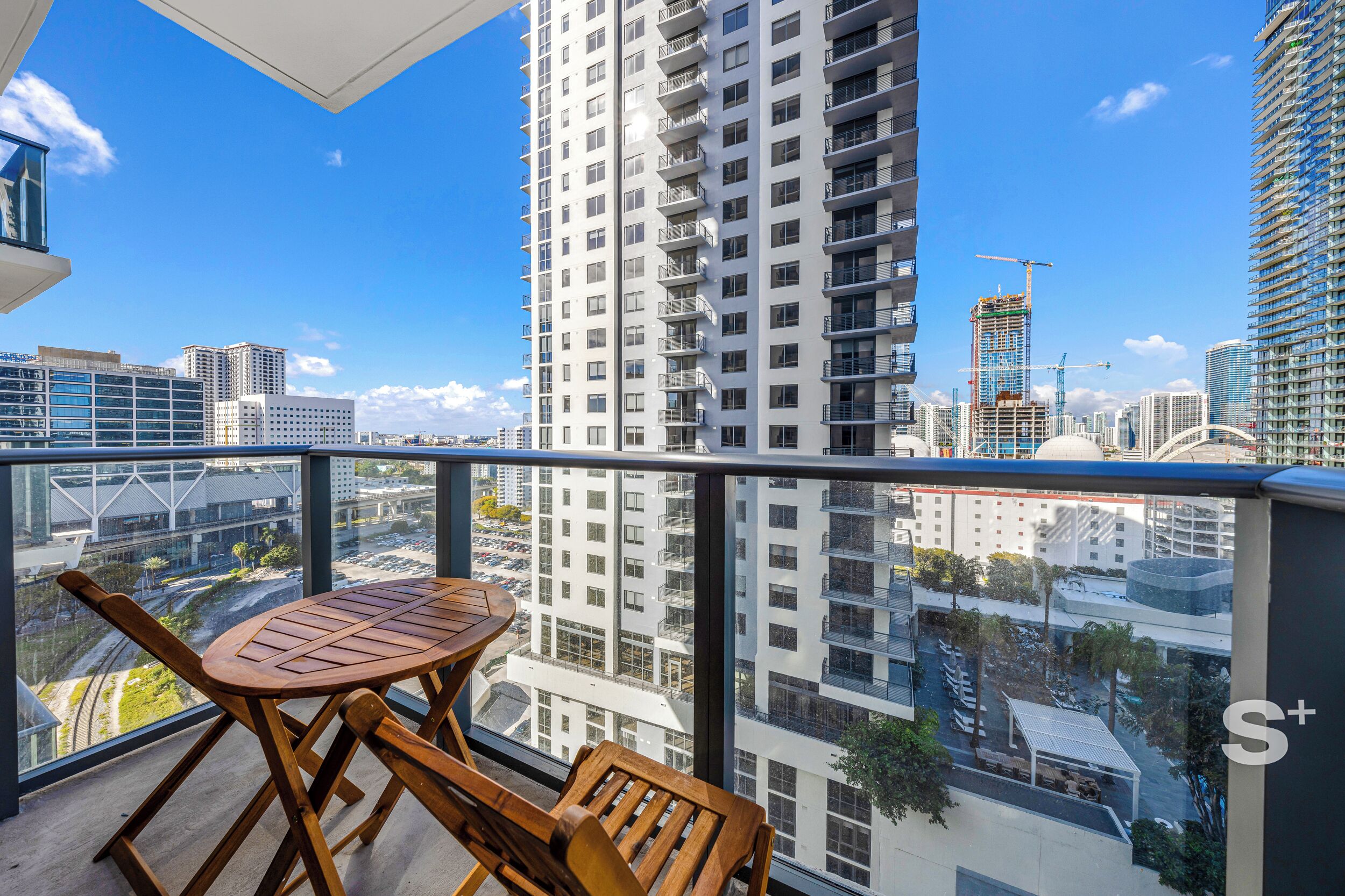 A balcony with a table and chairs, overlooking a cityscape with high-rise buildings and construction cranes.