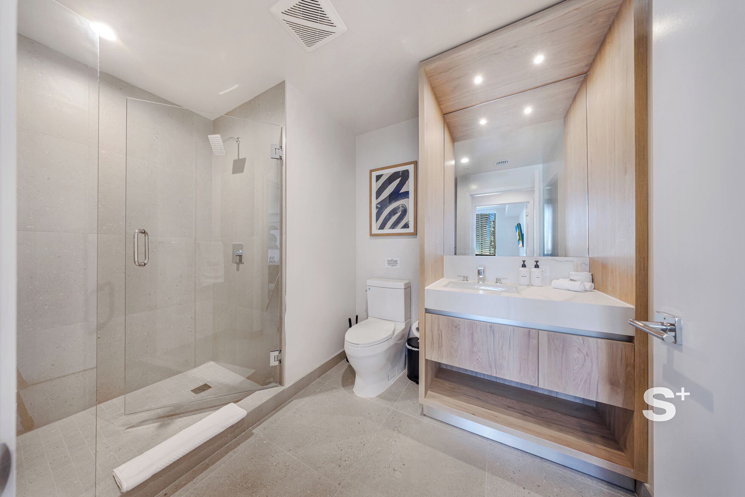 Un baño moderno con ducha de mampara de vidrio, inodoro y tocador con espejo.