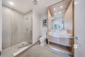 Une salle de bain moderne avec une douche à parois de verre, des toilettes et un meuble-lavabo avec un miroir.