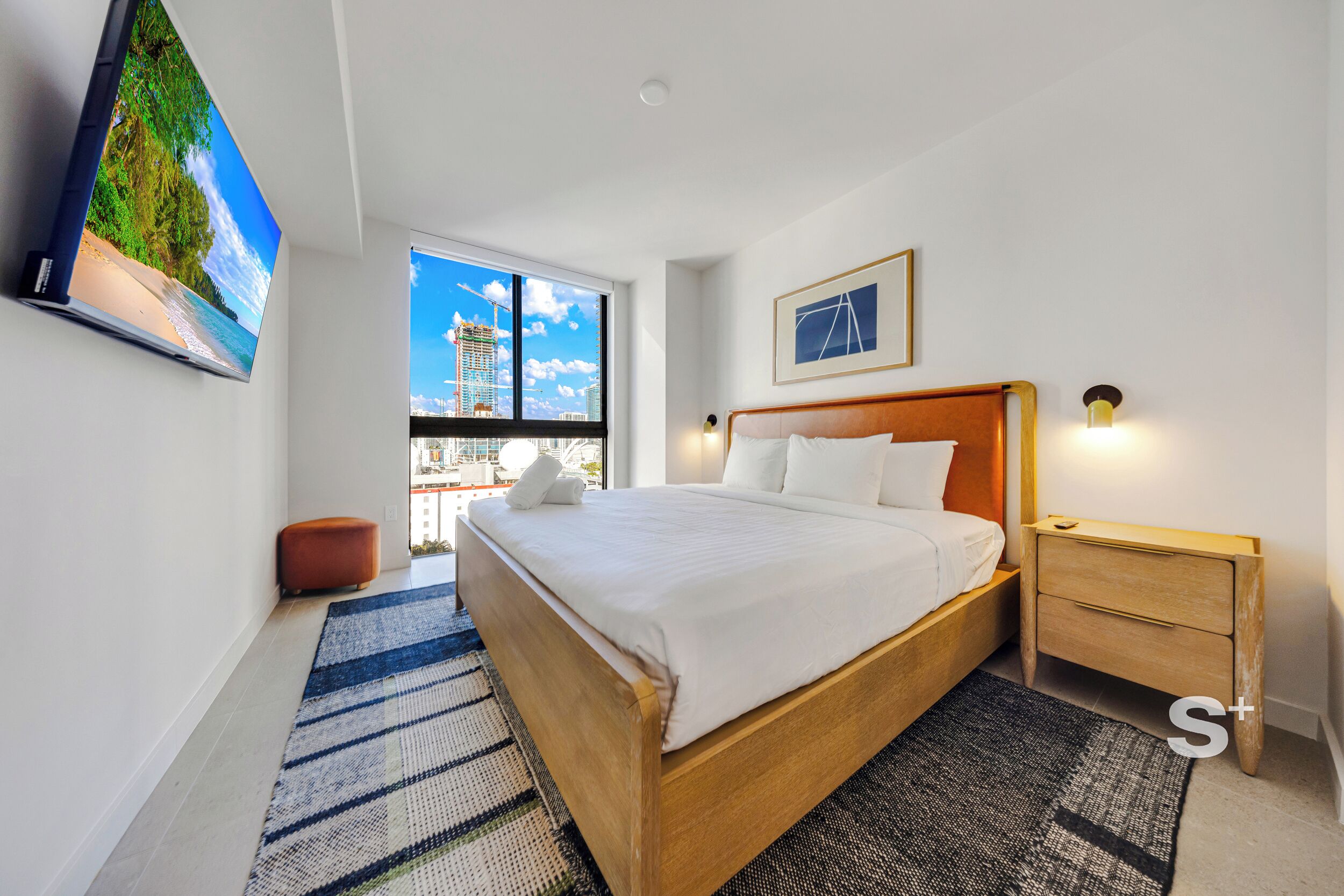 Camera d'albergo moderna con un letto grande, un comodino, una TV a parete e una finestra vista città.