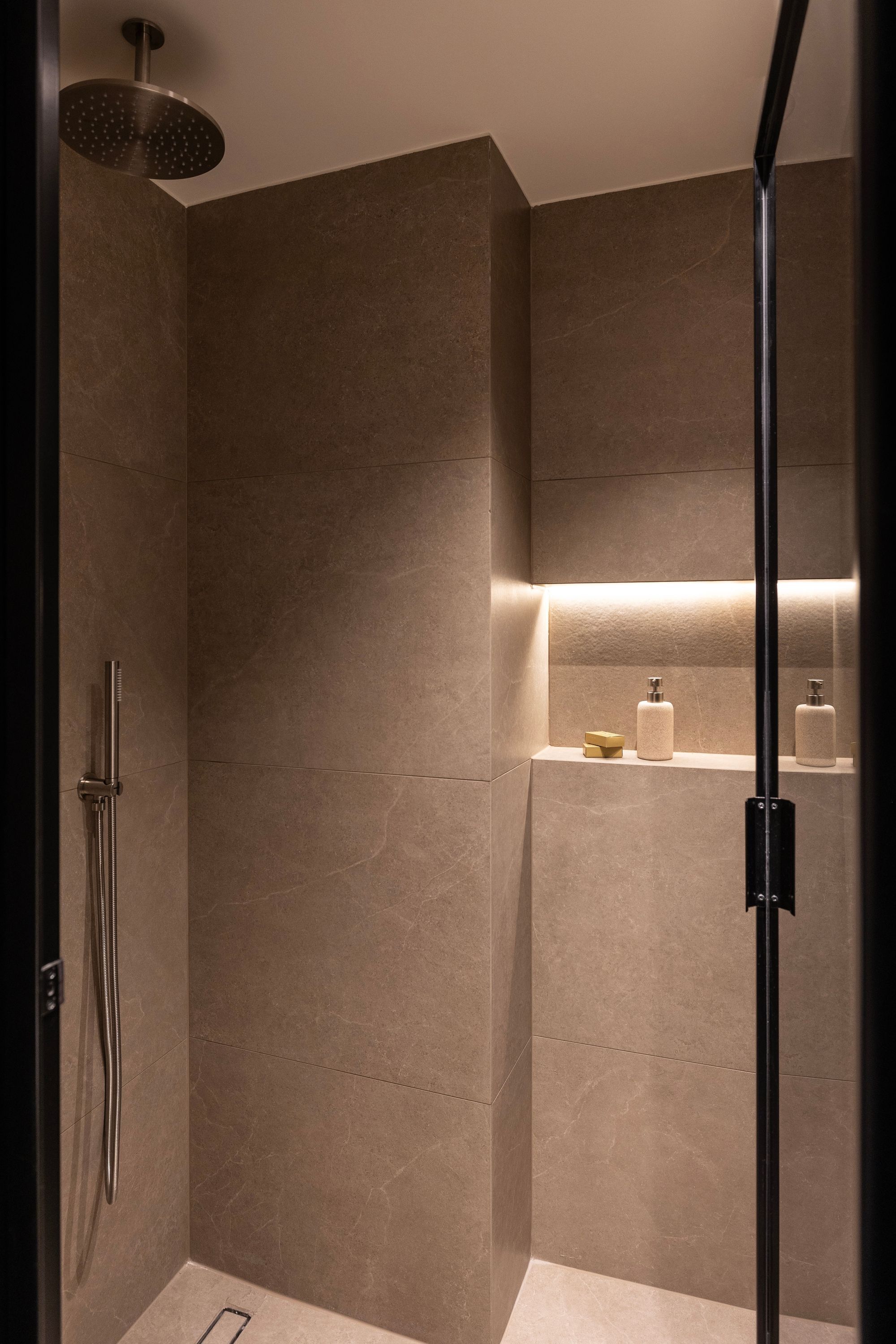 A modern bathroom with a walk-in shower, a glass door, and a shelf with toiletries.