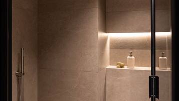 A modern bathroom with a walk-in shower, a glass door, and a shelf with toiletries.