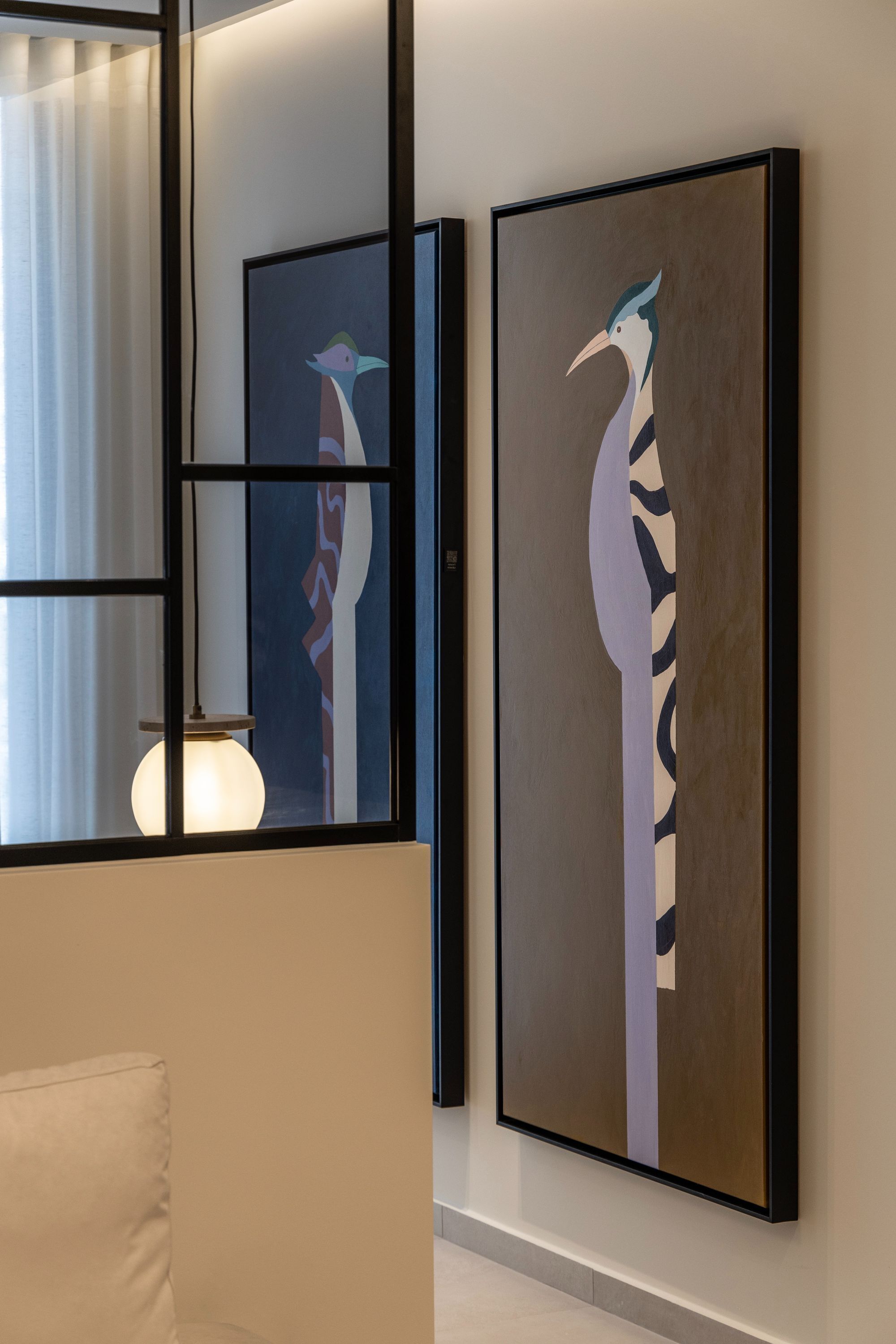 Two framed abstract paintings on a wall, a window with a curtain, and a light fixture.