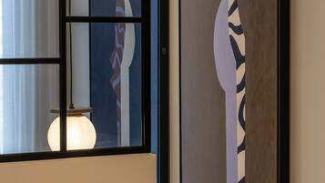 Two framed abstract paintings on a wall, a window with a curtain, and a light fixture.