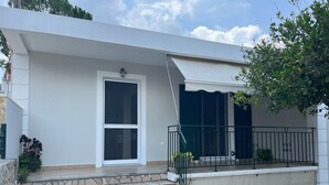 Une maison moderne à l’extérieur blanc, avec un escalier en pierre menant à un porche couvert et une rambarde en métal vert.