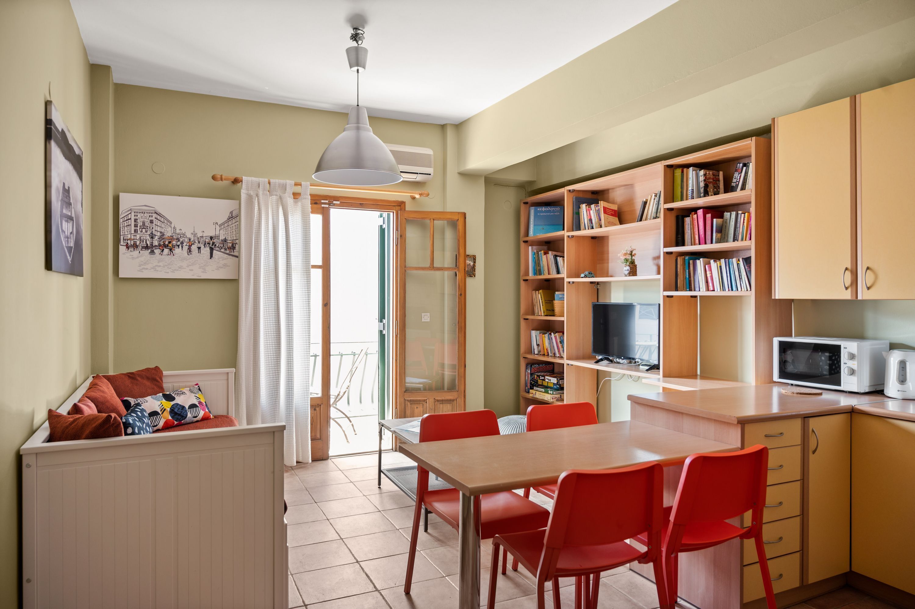 Een gezellige keuken met een eethoek, met een houten tafel, rode stoelen, een witte hanglamp en een boekenplank vol boeken.