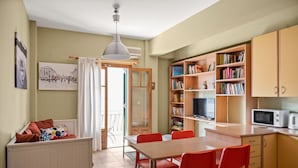 Eine gemütliche Küche mit Essbereich, ausgestattet mit einem Holztisch, roten Stühlen, einer weißen Pendelleuchte und einer Bücherwand voller Bücher.