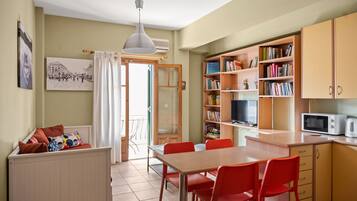 Een gezellige keuken met een eethoek, met een houten tafel, rode stoelen, een witte hanglamp en een boekenplank vol boeken.