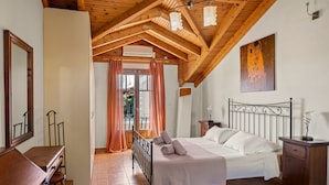 Ein Schlafzimmer mit einem Bett, Holzbalkendecke, einem Gemälde und einem Fenster mit Vorhängen.