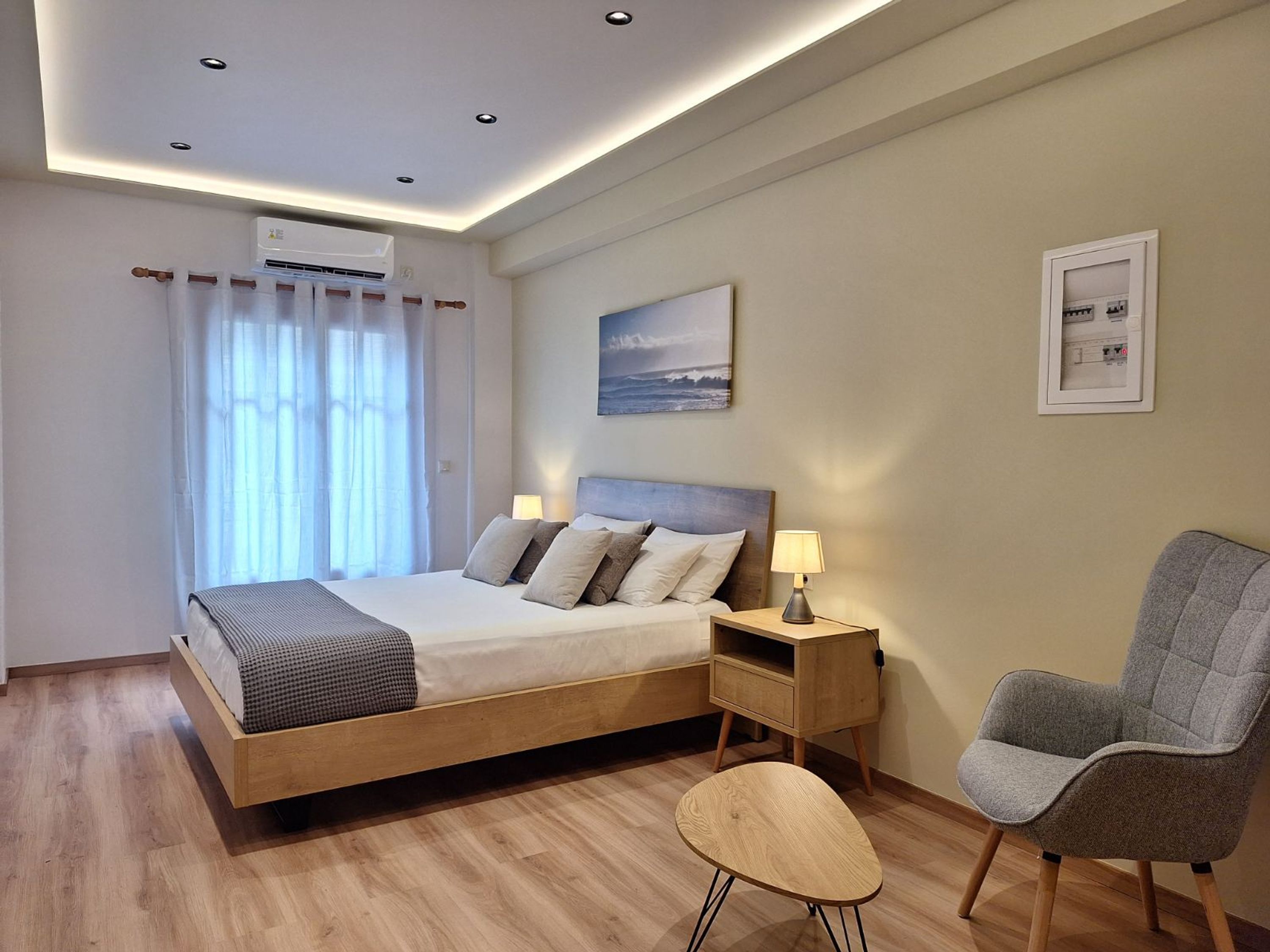 Une chambre d’hôtel moderne avec un lit en bois, une petite table, une chaise et un climatiseur fixé au plafond.