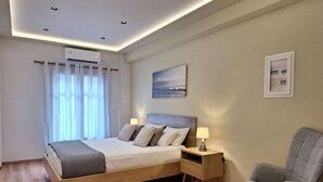 A modern hotel room with a wooden bed, a small table, a chair, and a ceiling-mounted air conditioner.