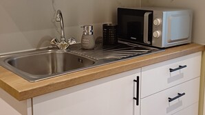 A modern kitchen with white cabinets, a stainless steel sink, a microwave, and a coffee maker.