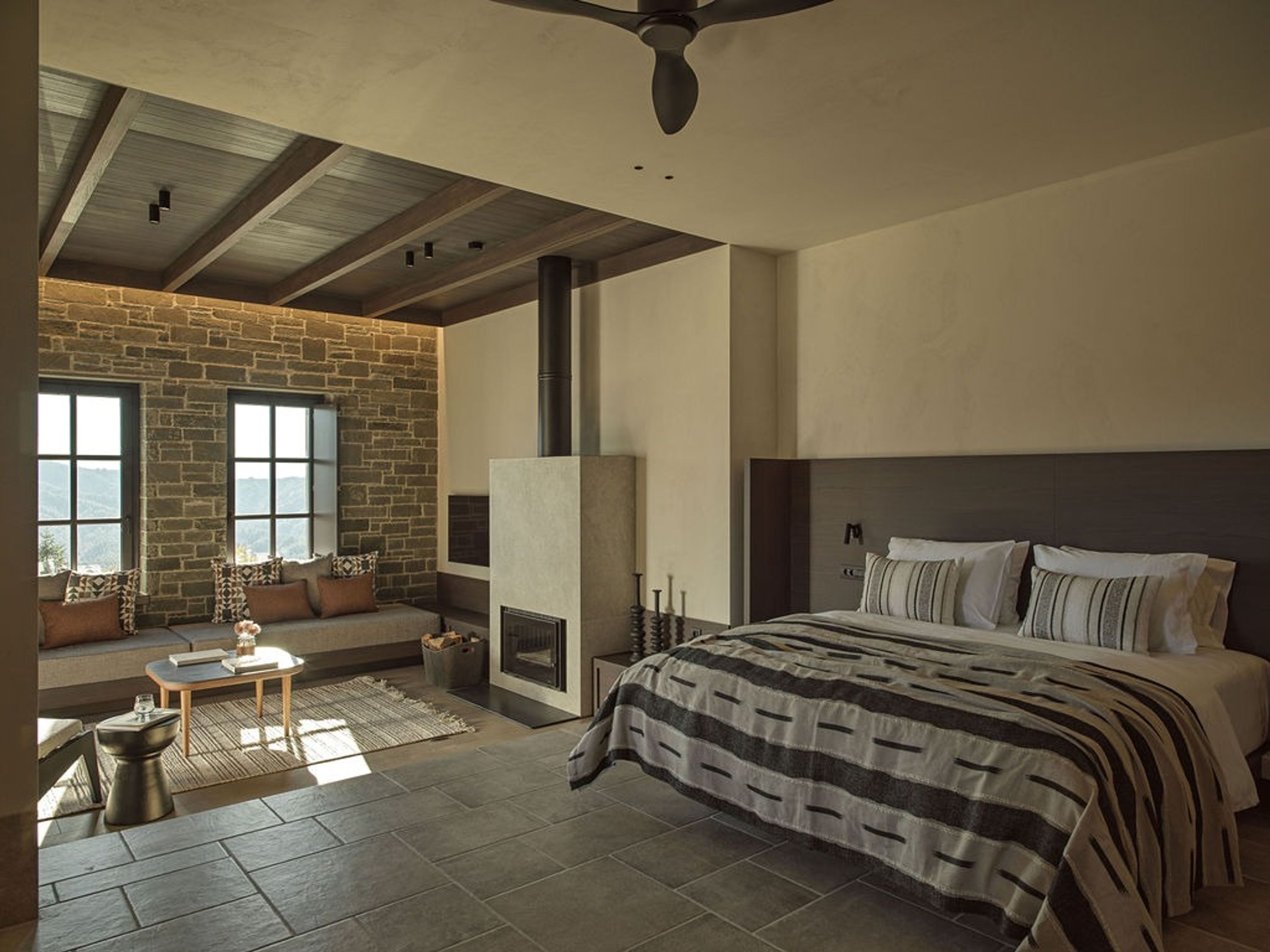 Un dormitorio con pared de piedra, chimenea, cama y vistas al exterior.