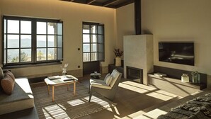 A spacious living room with large windows, a fireplace, and a television mounted on the wall.