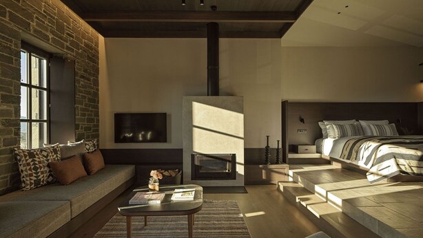 A modern living room with a fireplace, a sofa, a coffee table, and a bed with a headboard.