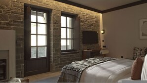 Een slaapkamer met een stenen muur, een open haard, een bed met dekbed, een nachtkastje en een aan de muur bevestigde televisie.