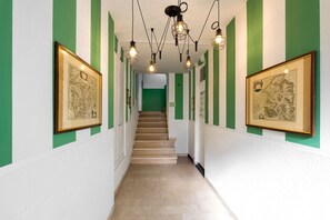 A hallway with green and white walls, framed pictures, a staircase, and hanging light fixtures. - Desenzano Suites - Achillea by Wonderful Italy (Desenzano del Garda)