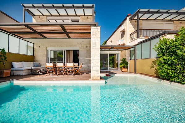 A modern outdoor pool area with a seating area, a pergola, and a stone wall. - Sunny Exclusive Ena in Chaniotis (Chaniotis)