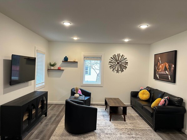 A living room with a flat-screen TV, black sofas, a coffee table, a decorative wall piece, and built-in shelves.