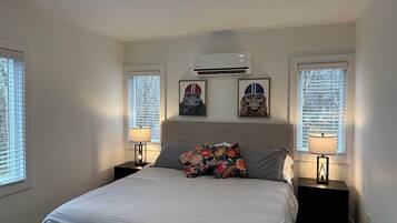 Un dormitorio con una cama, dos mesitas de noche, un cabecero y tres ventanas con persianas.