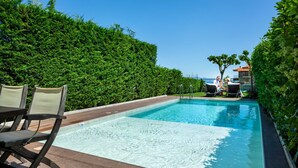 Una piscina amb una zona de fusta, cadires i una tanca de set.