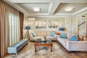 A living room with a sofa set, a bench, a coffee table, and artwork on the wall. - Sunny Exclusive Tria (Chaniotis)