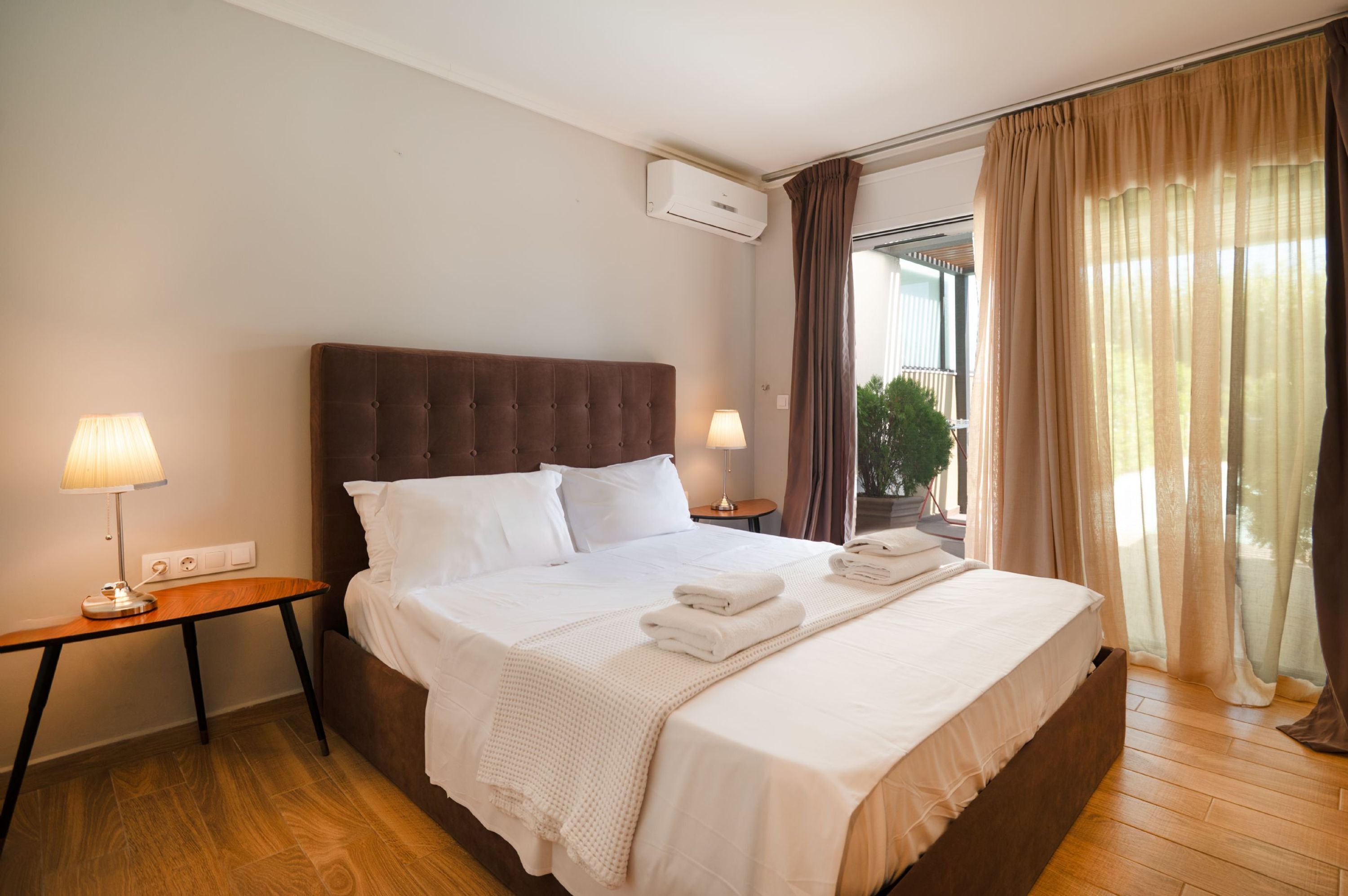 Une chambre d’hôtel avec un grand lit, deux tables de chevet avec des lampes, une fenêtre avec des rideaux et un appareil de climatisation fixé au mur.