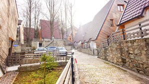Eine Kopfsteinpflasterstraße in einer historischen Stadt mit Steinbauten, einem Holzzaun und geparkten Autos.
