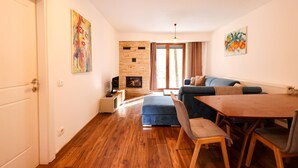 Ein modernes Wohnzimmer mit Holzboden, einer Couch, einem Esstisch mit Stühlen, einem Kamin und Kunstwerken an den Wänden.