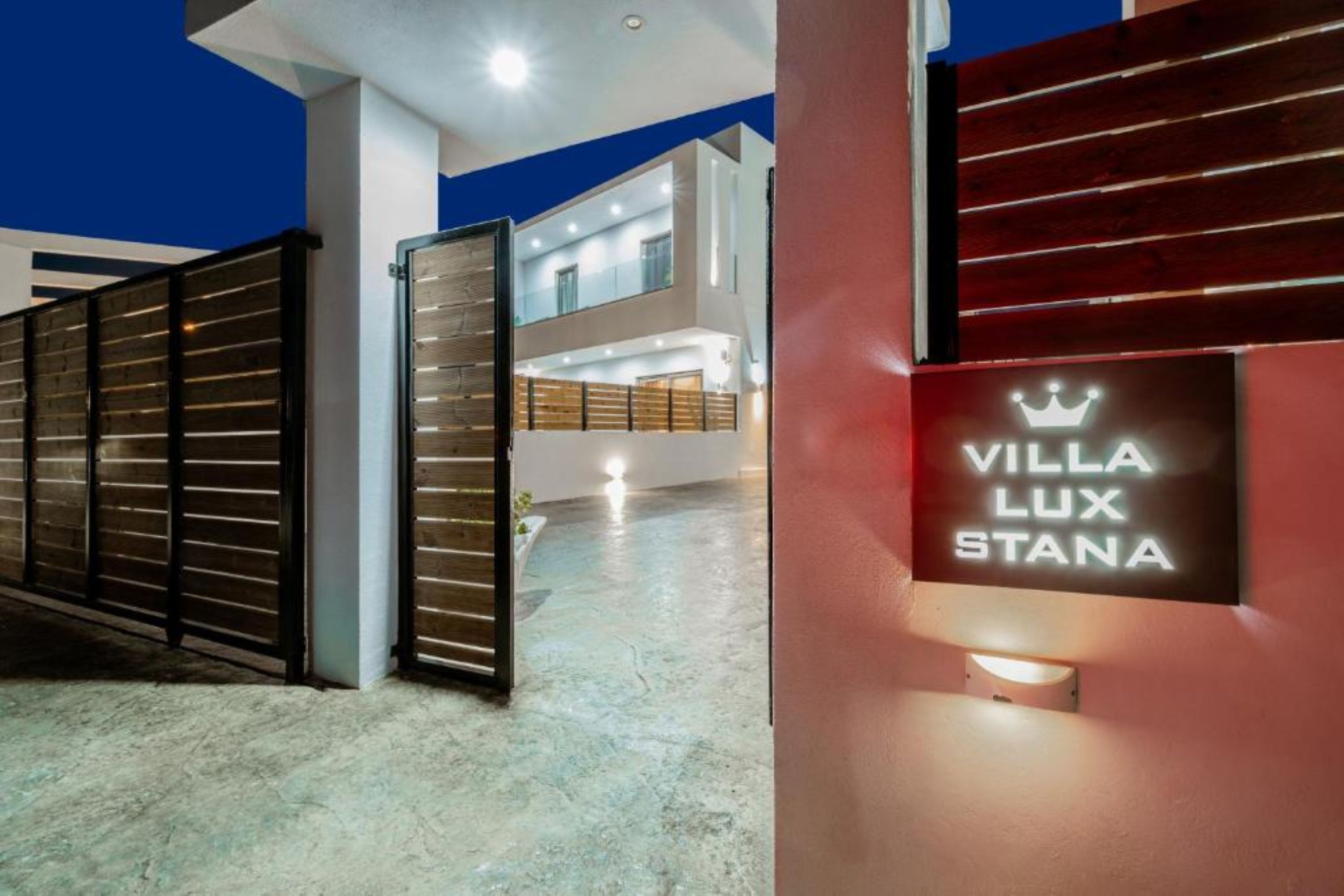 Une villa moderne, avec une plaque indiquant « VILLA LUX STANA », une entrée sécurisée par un portail et un intérieur à plusieurs niveaux, baigné de lumière.