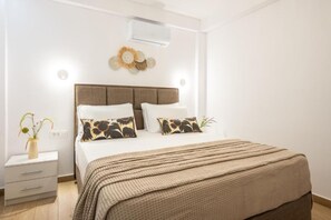 A bedroom with a bed, bedside tables, a wall-mounted air conditioner, and a decorative wall piece. - Villa Lux Stana II in Zakynthos (Laganas)