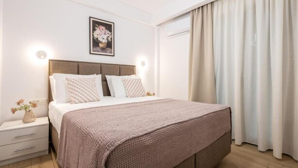 A bedroom with a bed, bedside tables, a nightstand, a framed picture on the wall, and a window with curtains. - Villa Lux Stana II in Zakynthos (Laganas)