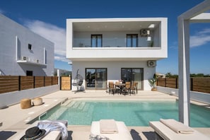 Ein modernes, zweistöckiges Haus mit Swimmingpool, Außenmöbeln und einem Balkon.