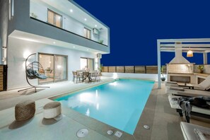 Ein moderner Poolbereich mit klarem Pool, Liegestühlen und einer Essgruppe.