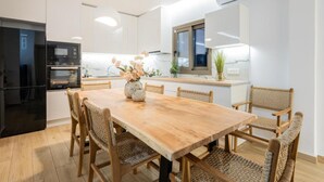 A modern kitchen with a wooden dining table and wicker chairs, a built-in oven, and a window with a view. - Villa Lux Stana II in Zakynthos (Laganas)