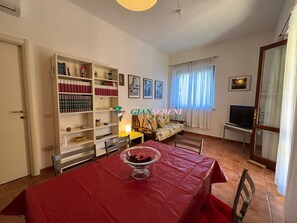 A living room with a red table, a sofa, a TV, and a bookshelf. - 4 sleeping places with garden – Ref. Casa Elena-Rif. CasaElena (Campiglia Marittima)