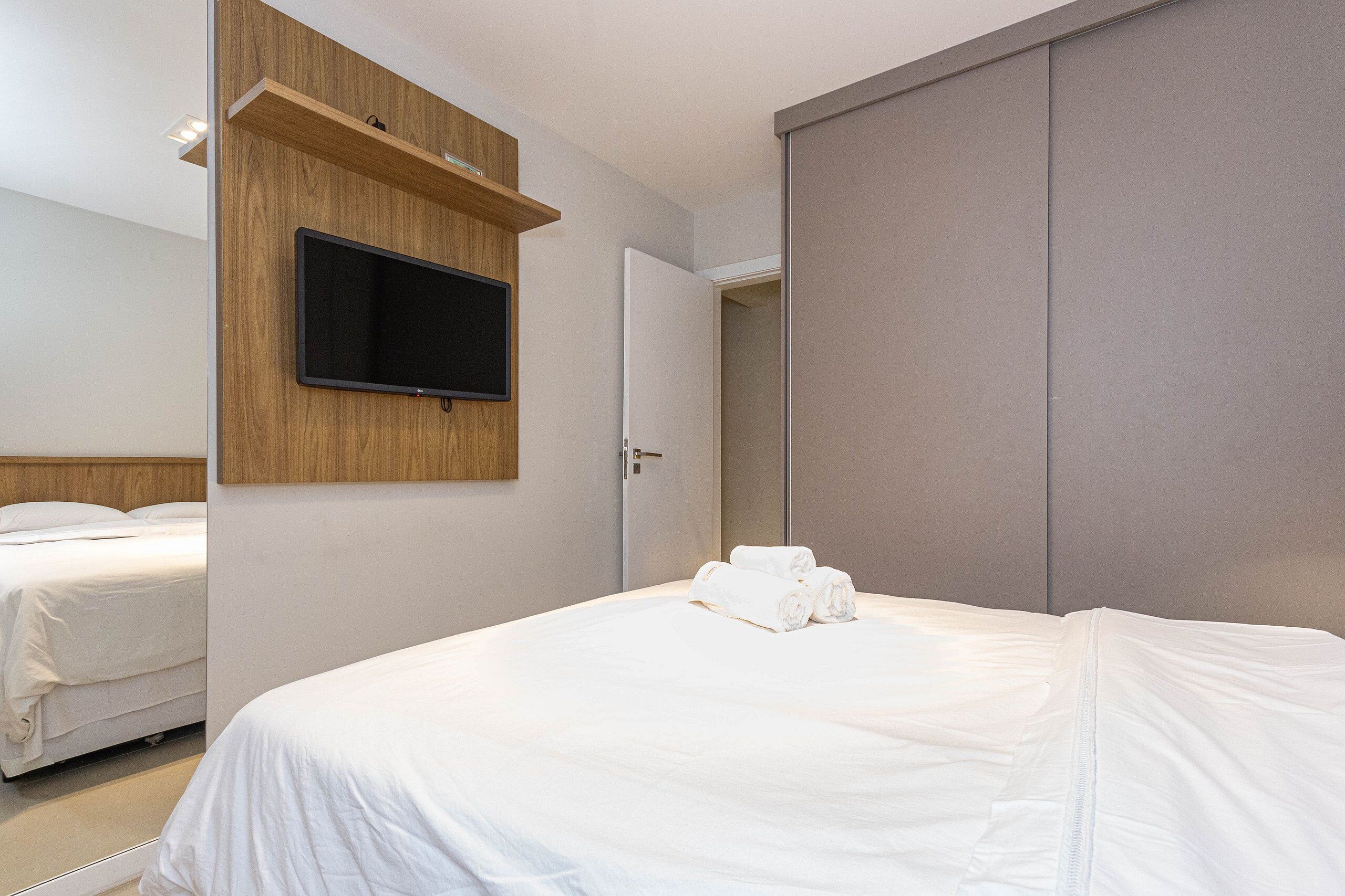 A hotel room with a bed, a TV mounted on a wooden panel, and a wardrobe.