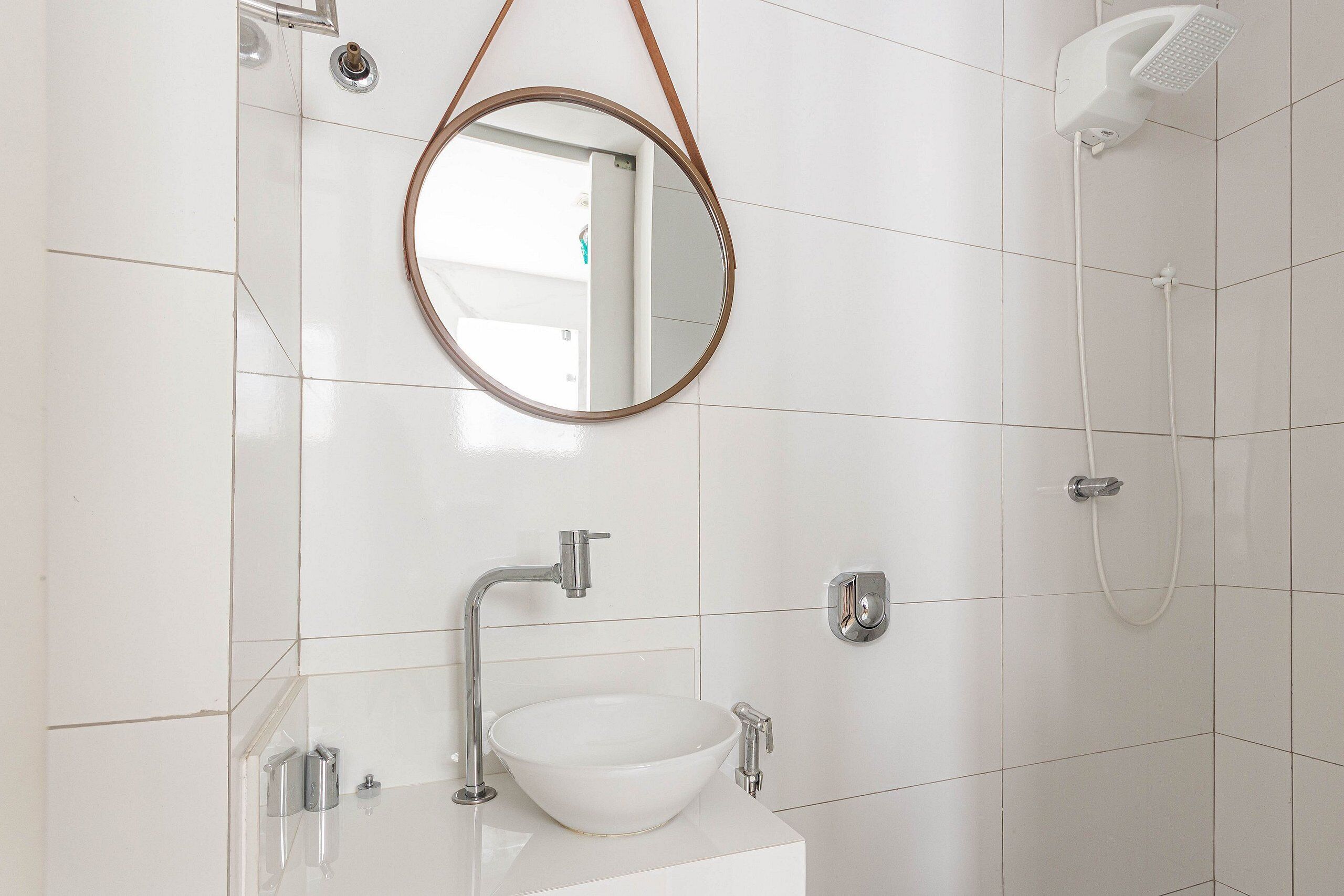 A bathroom with a white sink, a round mirror, and a shower.