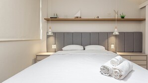 A modern bedroom with a large bed, bedside tables, a headboard, and a shelf with decorative items. - Apartamento Primavera (Rio de Janeiro)