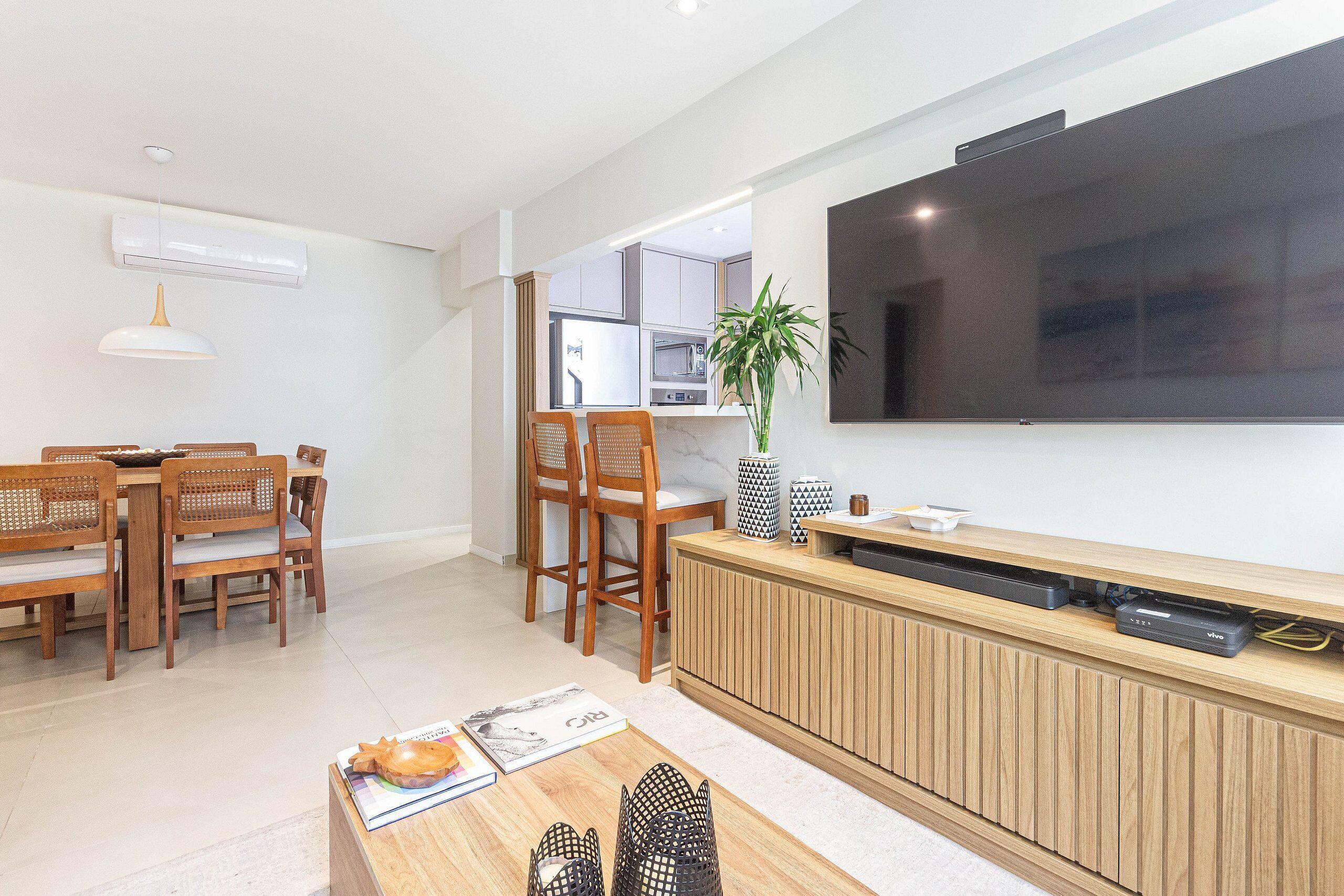 Una sala de estar moderna con comedor, muebles de madera, televisor de pantalla plana y cocina al fondo.