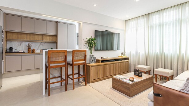 A modern living room with a sofa, coffee table, and two wooden chairs. A TV is mounted on the wall, and there's a kitchen area with cabinets and a countertop. - Apartamento Primavera (Rio de Janeiro)
