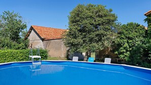 Una piscina azul cristalina con un trampolín, rodeada de vegetación y un edificio con techo rojo.