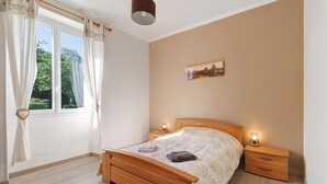 Un dormitorio con cama de madera, mesitas de noche, una ventana con cortinas y un cuadro en la pared.