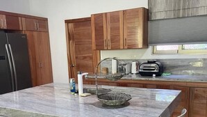 Een moderne keuken met houten kastjes, een marmeren eiland met barkrukken, een koelkast en een inbouwoven.