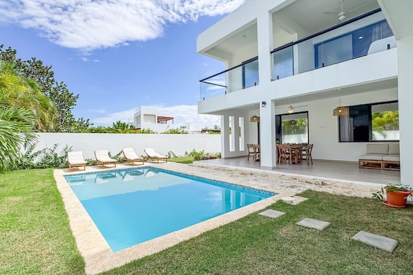 Una casa moderna a due piani con piscina, area salotto esterna e giardino curato.