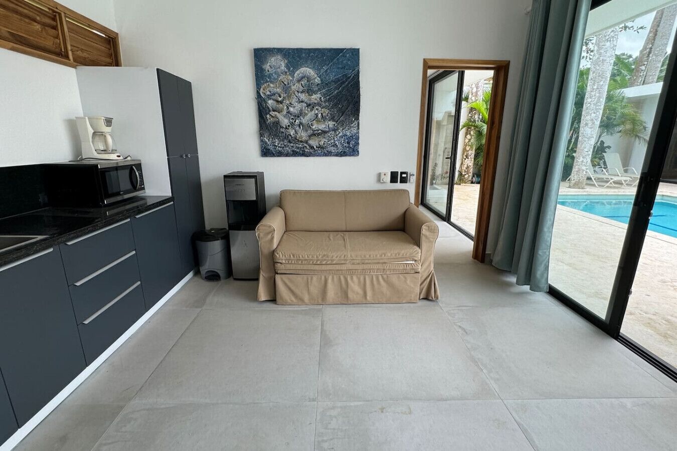A modern living room with a beige sofa, a coffee machine, a microwave, and a painting on the wall.