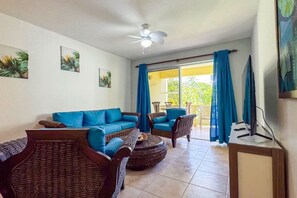 A living room with a blue sofa, wicker chairs, a ceiling fan, and a view of greenery through the window. - Renaissance Residence Cabarete (Cabarete)