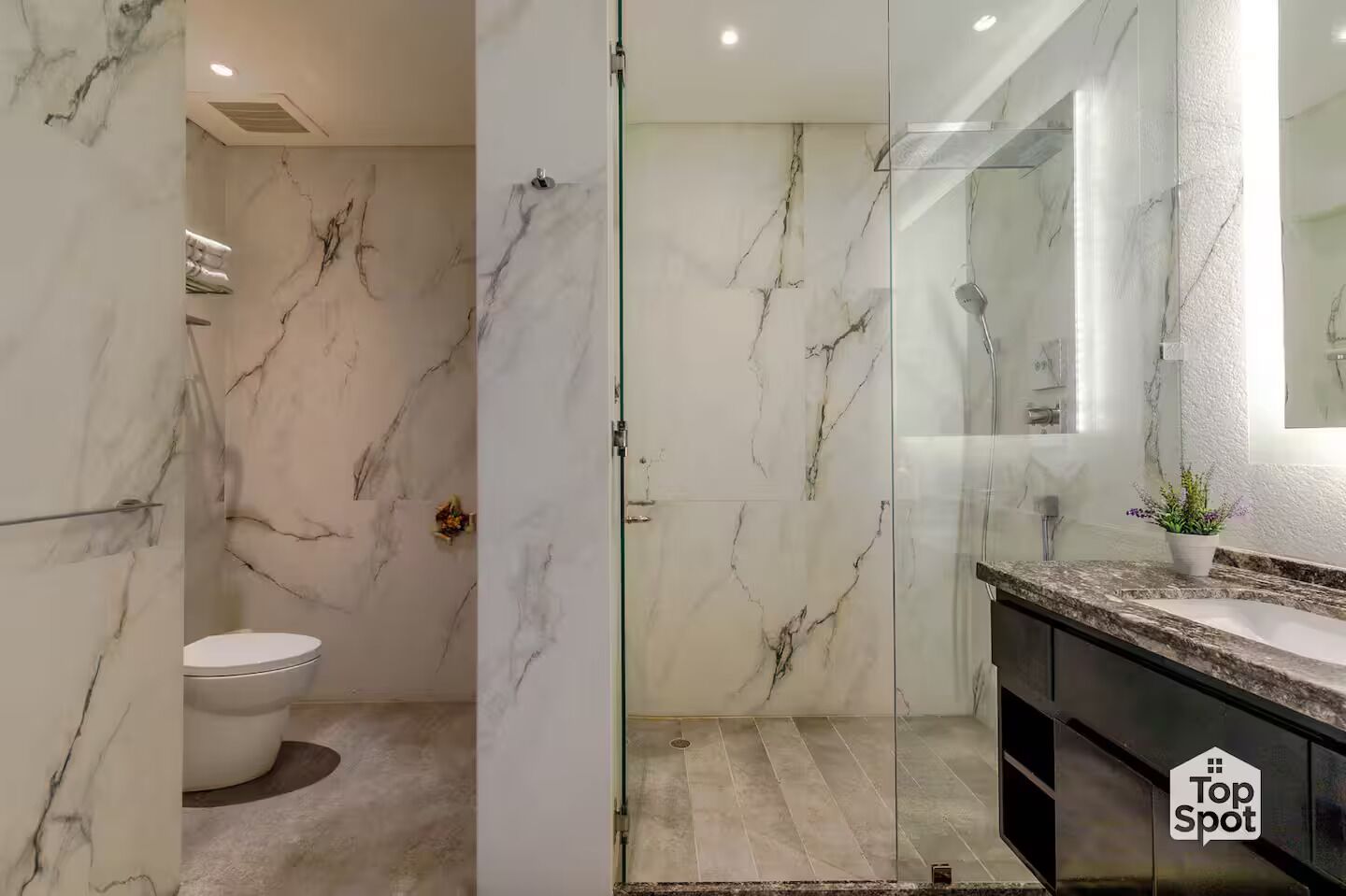 A modern bathroom with marble walls, a glass shower enclosure, and a granite countertop.